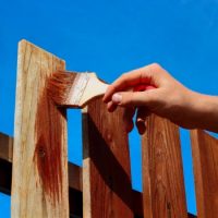 Man staining fence to help preserve and protect it from moisture