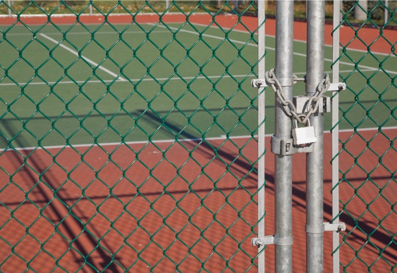 A padlocked chain link fence around a tennis field