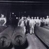Contractors standing behind giant rolls of chain wire mesh, some of the first chain-link fencing produced in Central Illinois